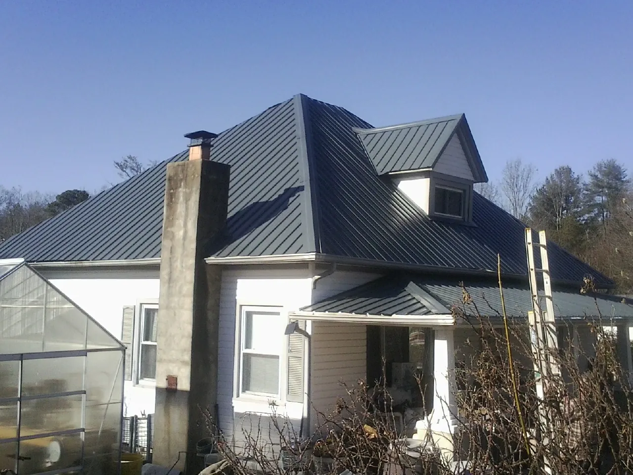 Dark blue standing seam metal roof on a white farmhouse with dormer — Slate & Tile Roof Repair by Roofing Brothers in Chevy Chase