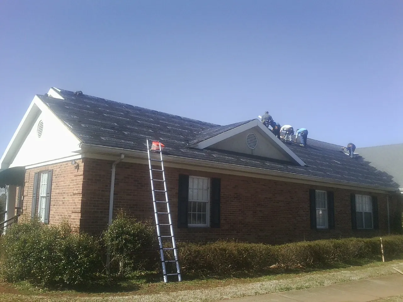 Crew tearing shingles off a brick ranch roof with a ladder set — Metal Roof Repair work by our crew in Chevy Chase
