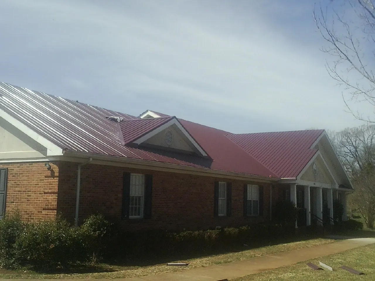 Red metal roof with gabled entries on a long brick building, from a Hail Damage Roof Repair job in Chevy Chase