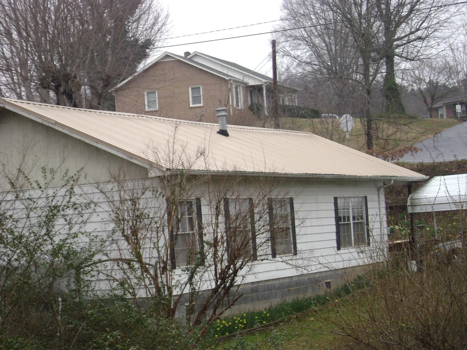 Tan metal roof on a white sided house set into a hillside — Commercial Roofing by Roofing Brothers in Chevy Chase